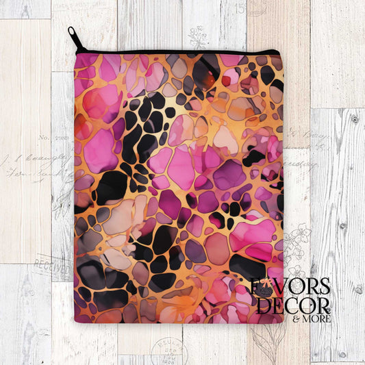 Padded book sleeve featuring an abstract cheetah print in shades of magenta, pink, plum, and gold with a zipper closure, shown on a wood background with Favors Decor & More logo.
