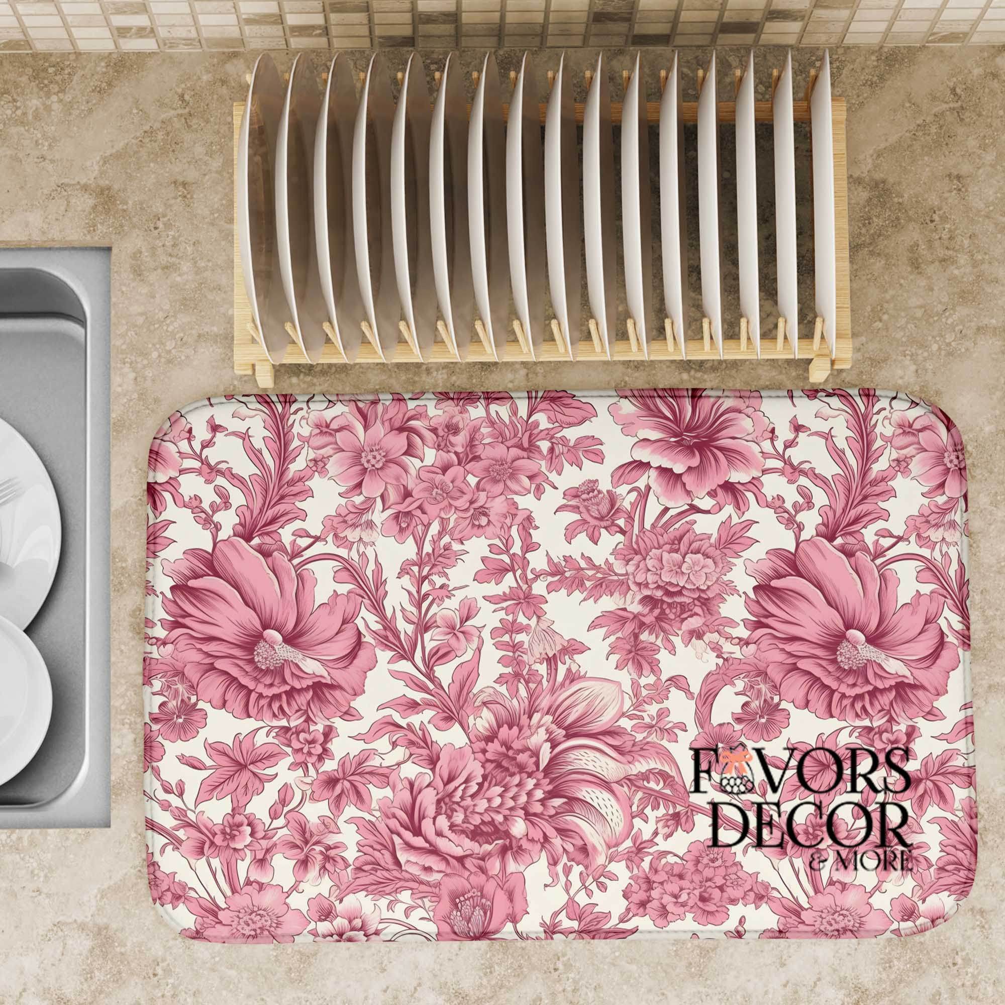 Blush pink floral dish drying mat on a kitchen counter with a dish rack and neutral tile backsplash.