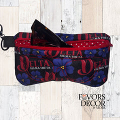 Delta Sigma Theta eyeglass pouch with red zipper, featuring purple African violets and DST logos on a black background, shown holding a pair of Tom Ford sunglasses (not included).