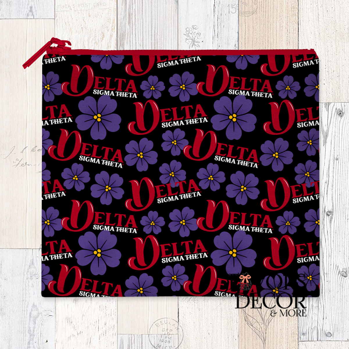  A reusable sandwich pouch with a black background featuring a repeating pattern of the word "DELTA" in red, "SIGMA THETA" in smaller white text, and purple African Violet flowers. The pouch has a red zipper.