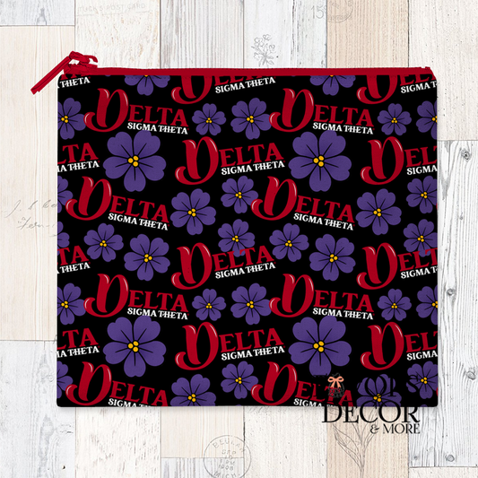  A reusable sandwich pouch with a black background featuring a repeating pattern of the word "DELTA" in red, "SIGMA THETA" in smaller white text, and purple African Violet flowers. The pouch has a red zipper.