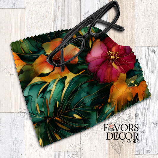 Tropical floral microfiber lens cleaning cloth with vibrant green leaves and bold pink, orange, and yellow flowers, displayed with black eyeglasses on top.