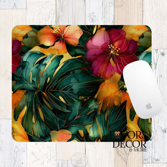 Mouse pad featuring deep green monstera leaves and tropical hibiscus flowers in orange, red, and pink, with gold accents in an alcohol ink art style. Displayed with a white Apple Magic Mouse and Favors Decor & More logo.