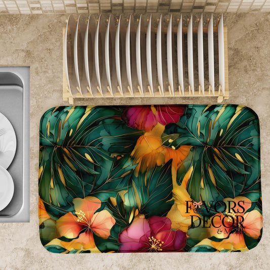 Tropical dish drying mat with dark green monstera leaves, golden foliage, and vibrant fuchsia and orange hibiscus flowers, shown displayed on a countertop with clean  dishes.