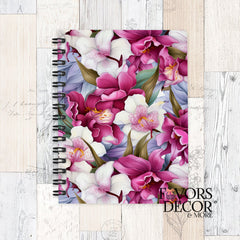 Spiral notebook with vibrant magenta and cream orchid floral design on the cover, set on a rustic whitewashed wood background with “Favors Decor &amp; More” logo