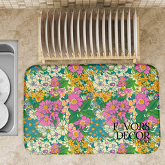 Dish drying mat with colorful vintage-inspired floral design in pink, yellow, teal, and cream, styled on a kitchen counter with a dish rack.