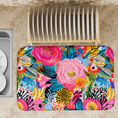 Colorful dish drying mat with bright hand-drawn florals in pink, yellow, blue, and coral on a neutral kitchen counter.