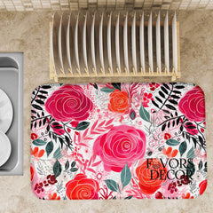 Dish drying mat with printed hand-painted pink and red roses and green leaves on a kitchen countertop near a wooden dish rack.
