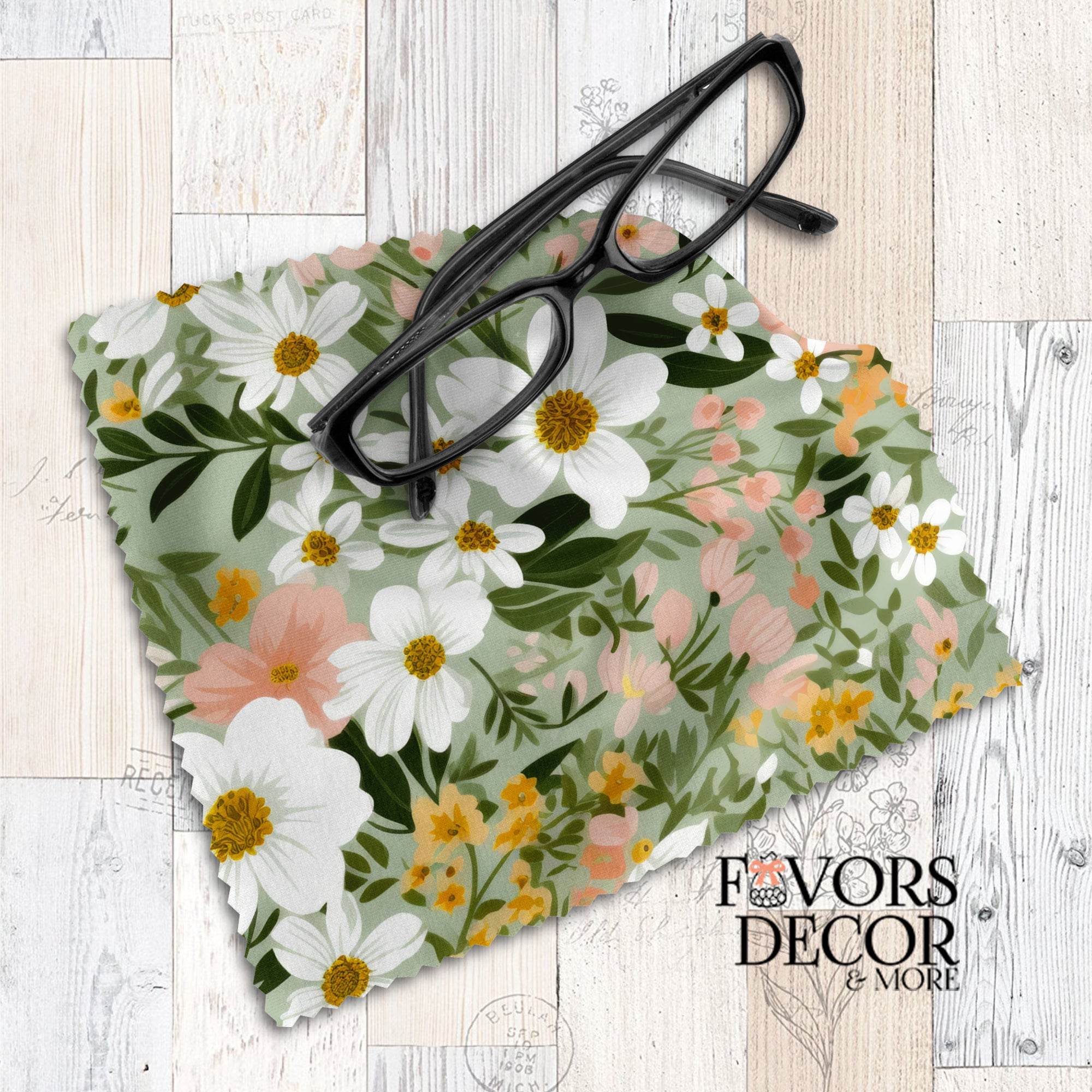 Soft meadow-inspired floral lens cloth with white, blush, and yellow flowers on a green background, styled with black eyeglasses.