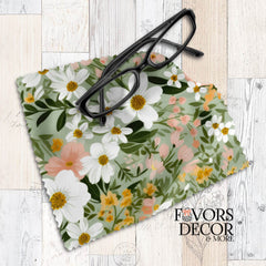 Soft meadow-inspired floral lens cloth with white, blush, and yellow flowers on a green background, styled with black eyeglasses.