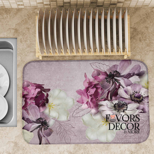 Dish drying mat with purple, blush, and cream watercolor florals on a lavender background, placed next to a sink and dish rack, Favors Decor &amp; More branding shown.