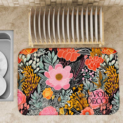 Dish drying mat with bright hand-drawn florals in coral, pink, gold, and mint on a black background, styled on a kitchen countertop.